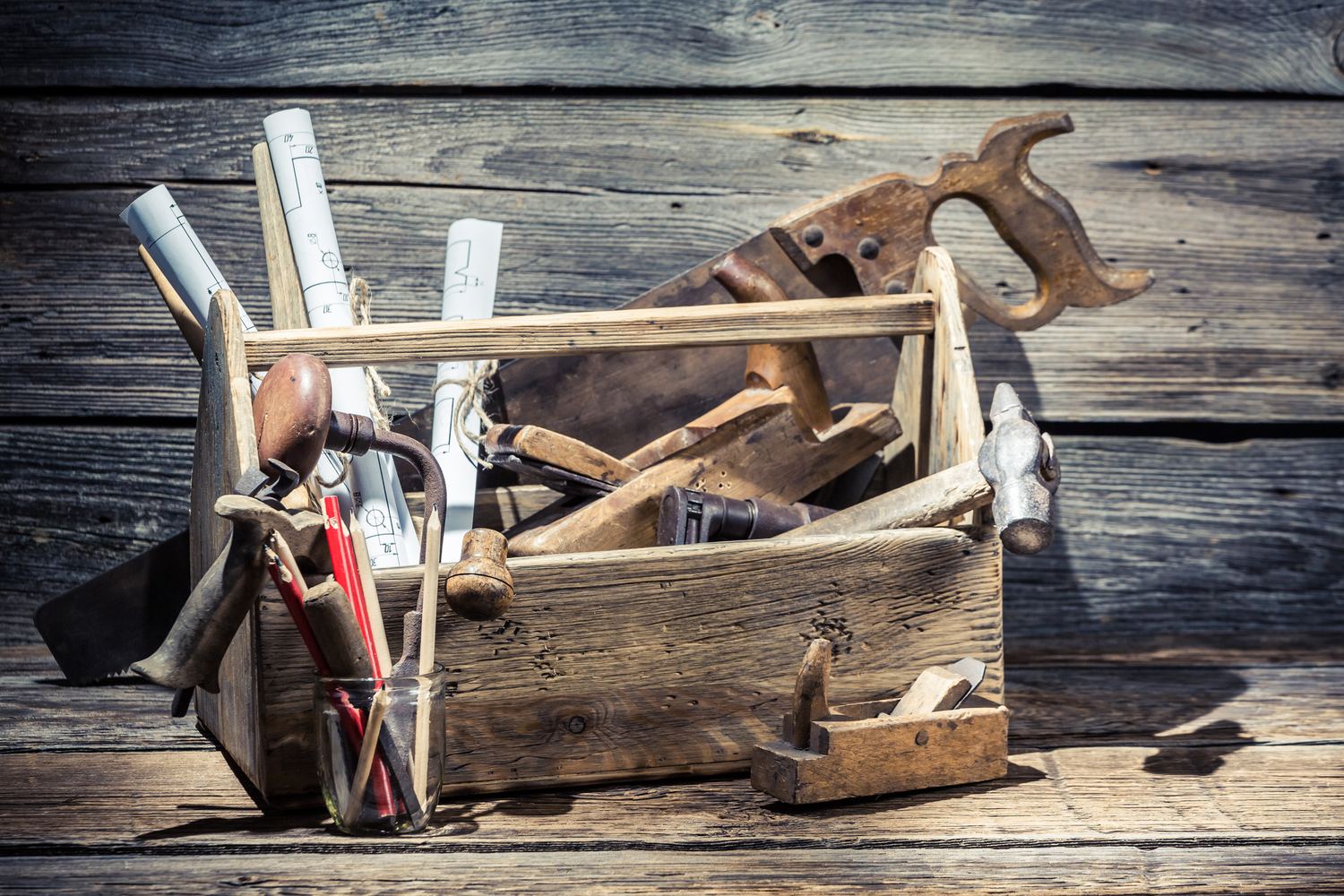 A worn wooden toolbox holding hand tools and rolled drawings